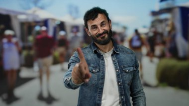 Sokak ortasında sakallı İspanyol bir adam. Çevresi insanlarla çevrili, hareketli şehir ortamında parmağıyla hareket etmiyor..