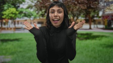 Siyah spor elbiseli genç İspanyol kadın güneş ışığı altında binanın ön cephesinde el çırpıyor..