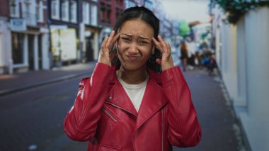 Şehrin sokaklarında baş ağrısı için tapınak basan genç İspanyol kadın kırmızı deri ceket ve beyaz tişört giyiyor..