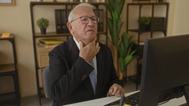 Takım elbiseli kıdemli bir adam ofis masasında otururken boğaza dokunurken ve bilgisayarın başında öksürürken iç mekanda iş ortamını hazırlarken rahatsız görünüyor.