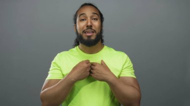 Stüdyoda gri arka plan ve neon yeşil tişörtle görülebilen el hareketlerini ve avuçlarını gösteren bir adam..