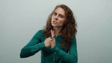 Öfkesini ifade eden bir kadın, beyaz arka plana karşı agresif bir tavırla hareket ediyor kıvırcık saçlı yeşil bir kazak giyiyor ve kafkas görünümlü izole bir ortamda hayal kırıklığını canlı bir şekilde tasvir ediyor.