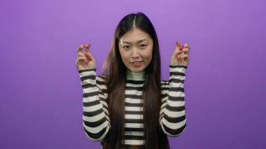 Tırnak işareti yapan bir kadın mor bir arka plana karşı iki eliyle hareket ediyor, çizgili gömlek giyiyor, alaycılık ya da ironi yapıyor, uzun saçlı ve gündelik ifadeli..