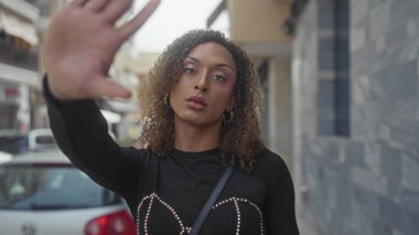 Kadın, taştan bir binanın yanındaki dar bir şehir sokağında dur işareti yaparak elini uzatıyor..