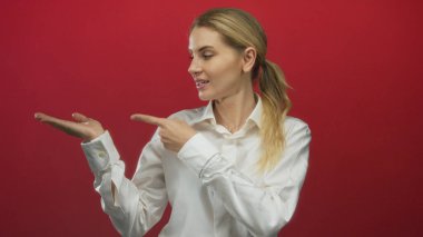 Avuç içini gösteren hareketler canlı kırmızı arkaplan karşısında açık sarı saçlı beyaz gömlek giyen bir kadın.
