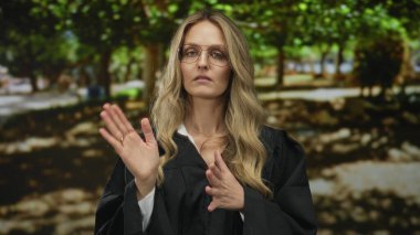 Parkta el ele tutuşan bir kadın, yeşil yeşillik arka planda üniforma giyen sarışın bir yargıcın yanında el ele tutuşuyor..