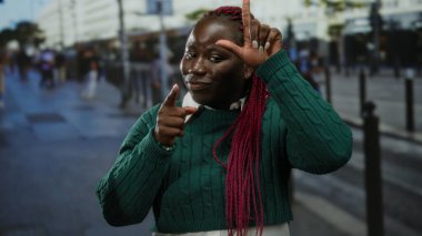 Örgülü bir kadın ezik jestler yapıyor ve şehir caddesinde canlı bir şehir ortamında kameraya bakıyor..