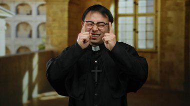 Asyalı rahip tarihi kilise avlusunda gülümsüyor, dışarıdaki ortamlarda sıcaklık ve maneviyat saçıyor, dini imalarla davetkar ve sakin bir atmosfer yaratıyor..