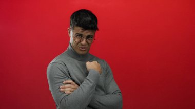 Genç İspanyol bir adam, parmaklarıyla kırmızı bir arkaplan karşısında hayır işareti yapıyor. Gri balıkçı yaka bir kazak içinde cazibe ve kendine güven yayıyor. Çekici bir gülümseme sergiliyor..