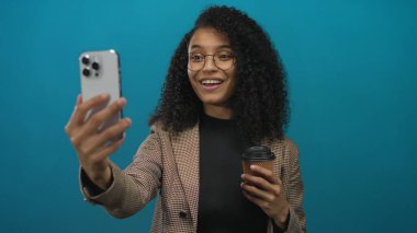 Stüdyo görüşmesi sırasında gülümseyen ve elinde akıllı telefon ve kahve fincanı tutan kadın; sosyal bağlantı mutluluğu.