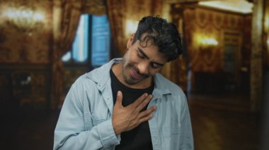 İspanyol adam, avizeler ve ağır kumaşlarla aydınlatılmış süslü otel binasında sağ elini göğsüne koyar..