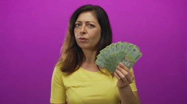 Orta yaşlı İspanyol bir kadın, bir stüdyoda mor bir fon karşısında bir deste Şili pesosu tutuyor. Sürpriz servet..