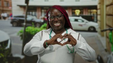 Steteskoplu bir kadın kalabalık şehir caddesini gösteriyor. Arabaları ve yayaları var. Canlı şehir hayatı sergiliyor..