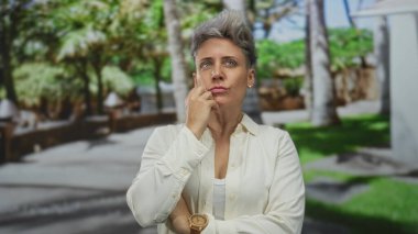 Beyaz gömlekli kadın ahşap saat ve çapraz kollar çene üzerinde yeşil orman sahnesi ortasında el ele; tefekkür.