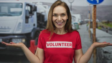 Gönüllü tişört giyen bir kadın, şehir sokaklarında el hareketlerini ve gülen yüzünü gösteriyor. Şefkat dayanışması..
