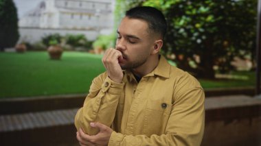 Genç İspanyol adam gün ışığında yosunlu taş bir avlunun yanında tırnaklarını yiyor..