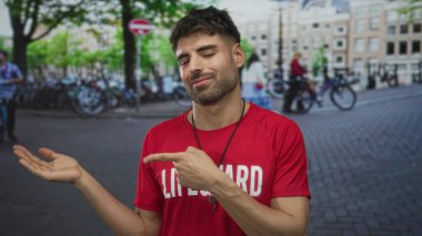 Kırmızı cankurtaran tişörtlü İspanyol genç adam park halindeki bisikletlerle dolu işlek kaldırım taşı caddesinde avuç içi kadar açık sunar; belirsizlik.