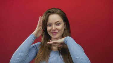 Kadın yüzü güzel ışıklandırılmış bir stüdyoda elleri ile canlı kırmızı bir duvara karşı, nazikçe gülümsüyor;.