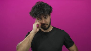 Sakallı genç İspanyol bir adam canlı pembe bir arka plana karşı düşünceli ve odaklanmış görünüyor..