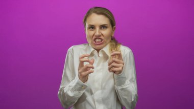 Yüzünde somurtkanlık ifade eden bir kadın canlı pembe bir arka plana karşı duruyor, beyaz gömlek giyiyor, duygu ve yoğunluğu vurguluyor..