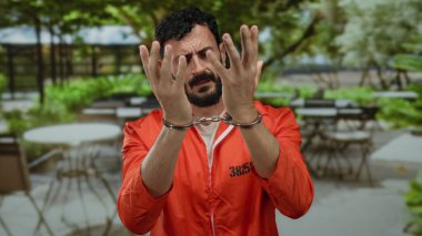 Hapishane tulumlu İspanyol adam, arka planda boş masalar olan bir lokantada kelepçeli bir şekilde perişan görünüyor..