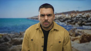 Kıyı portresi için güneşli kayalık kıyıya yakın stüdyoda kaşları çatık bir adam; ciddiyet.