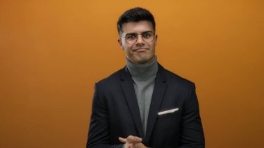 Gözlüklü ve balıkçı yakalı genç adam izole edilmiş turuncu bir arka plana karşı duruyor ve modern profesyonel bir hava yayıyor..