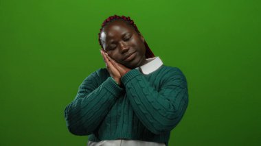 Yeşil süveter içinde huzur içinde dinlenen, dingin yeşil arka planda huzur ve sükunet taşıyan bir kadın.