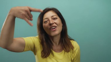 Kaya boynuzları yapan kadın, elleri havada, sarı tişörtlü, gök mavisi stüdyo ortamında, rock-fun metal enerjili..