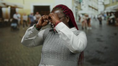 Dışarıda gülümseyen bir kadın, şehirde elleri gözlüklü ve örgülü bir süveterle dürbünlü jest yapıyor..