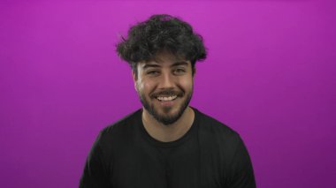 Sakallı İspanyol genç adam gülümsüyor ve kollarını pembe bir arka plana yaslıyor. Kendine güveni ve karizması var. Profesyonel ya da günlük kullanım için ideal..