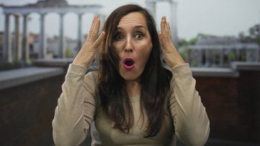 Roma harabelerinde sıkıntılı bir şekilde ayakta duran kadın arka planda tapınaklar ve eski mimari eserlerle görünür, dışa dönük yüzler ve gündelik giysiler sergiliyor..