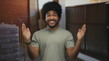 İnşaat alanında el kol hareketi yapan, kapalı alanda ölçüm yapan, günlük gömlek giyen, gülen, tuğla ve endüstriyel geçmişi olan bir adam.