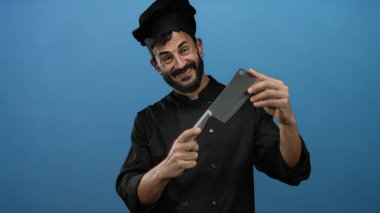 Sakallı İspanyol aşçı gülümsüyor ve mavi arka planda bir satırı tutuyor..