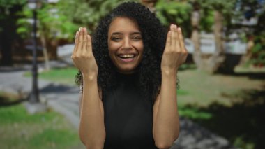 Yeşil bir park ortamında ellerini kaldırarak şaşırdığını ifade eden kadın oyuncu duygular ve doğa ile bağlantı sergiliyor.