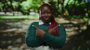 Pembe örgülü bir kadın yeşil bir kazak giyiyor. Parkta zıt yönlerde. Arka planda bulanık ağaçlar var..