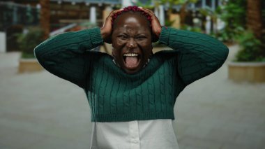 Yeşil kazaklı Afro-Amerikalı kadın şehir sokaklarında hayal kırıklığını ifade ediyor. Arka planı bulanık, stres ve duygu taşıyor..