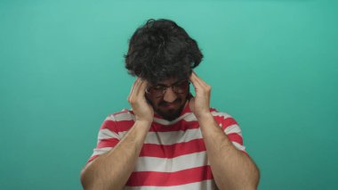 Çizgili gömlekli sakallı genç adam yeşil arka planda stresli görünüyor..