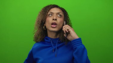 Mavi kapüşonlu kıvırcık saçlı transseksüel kadın yeşil stüdyoda akıllı telefonu kulağına tutuyor; belirsizlik..