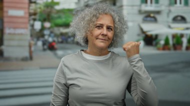 Kıvırcık saçlı, kendinden emin orta yaşlı kadın sokak ortamında dikiliyor, güç gösterisi yapıyor ve bağımsızlığını ilan ediyor..