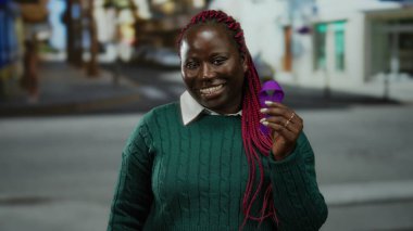 Mor kurdeleli bir kadın, şehir sokaklarında yeşil süveter içinde farkındalık ve toplum desteğini kutluyor..