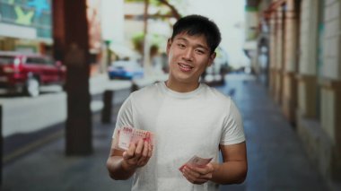Kalabalık bir şehir caddesinde Tayvan doları tutan genç adam, gün boyunca şehir dışında dururken gülümsüyor..