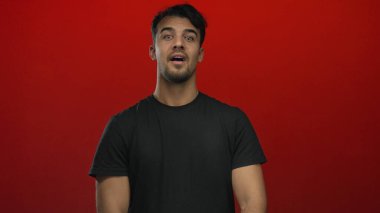 Siyah gömlekli İspanyol adam canlı kırmızı arka plana karşı mükemmel bir jest yapıyor. Kendine güvenen yüz ifadesinden haz ve memnuniyet duyuyor..