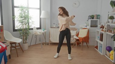 Güzel dekore edilmiş bir bebek odasında beşiği ve oyuncaklarıyla neşeyle dans eden genç bir kadın yumuşak doğal ışık altında neşeli ve neşeli bir atmosfer yaratıyor..