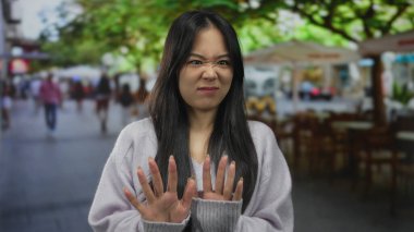 Kalabalık bir sokak terasında dikilen düşünceli genç Çinli kadın, insanlarla ve yeşilliklerle çevrili, canlı ve canlı bir açık hava manzarası yaratıyor..