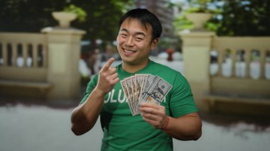 Açık havada gülümseyen genç adam şehir sokaklarında dolarları elinde tutuyor..