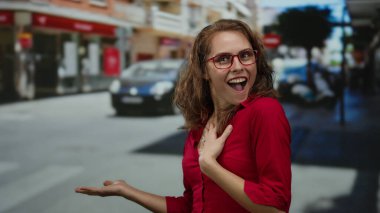 Kırmızı tişörtlü kadın şehir sokaklarında bulanık geçmişiyle heyecan verici jestler yapıyor. Arabalar ve binalar, gençlik enerjisi ve canlı şehir atmosferi..