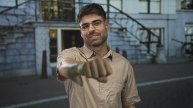 Gözlüklü ve kirli sakallı bir adam şehir sokaklarındaki izleyiciyi işaret ediyor..