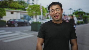 Siyah tişörtlü adam gülümsüyor ve şehir sokağında dikilirken dilini dışarı çıkarıyor. Bulanık arabalarla dolu. Neşeli neşe.