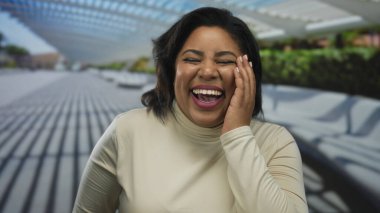 Modern bir şehir ortamında neşeli bir şekilde gülen kadın, şehir mimarisi ve doğal fon ile mutluluğu sergiliyor..